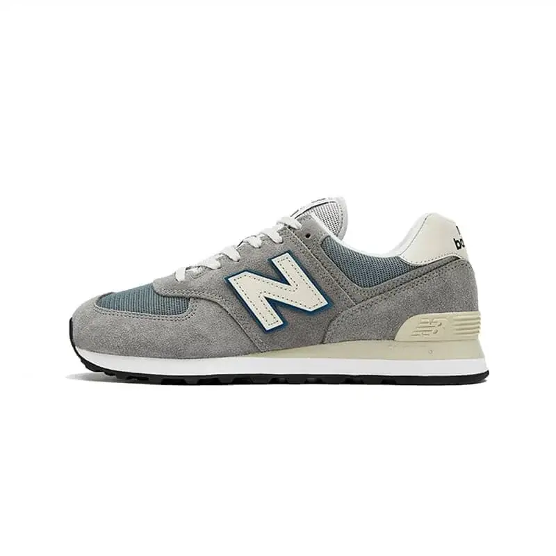 A classic New Balance 574 sneaker featuring a combination of gray suede and mesh, white laces, and a prominent blue-outlined “N” logo. The shoe has a cream midsole with a black outsole, offering a clean, versatile look perfect for everyday casual wear.